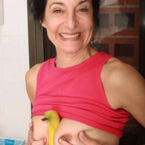 A mature woman undresses in her kitchen, teasing a banana near her intimate area